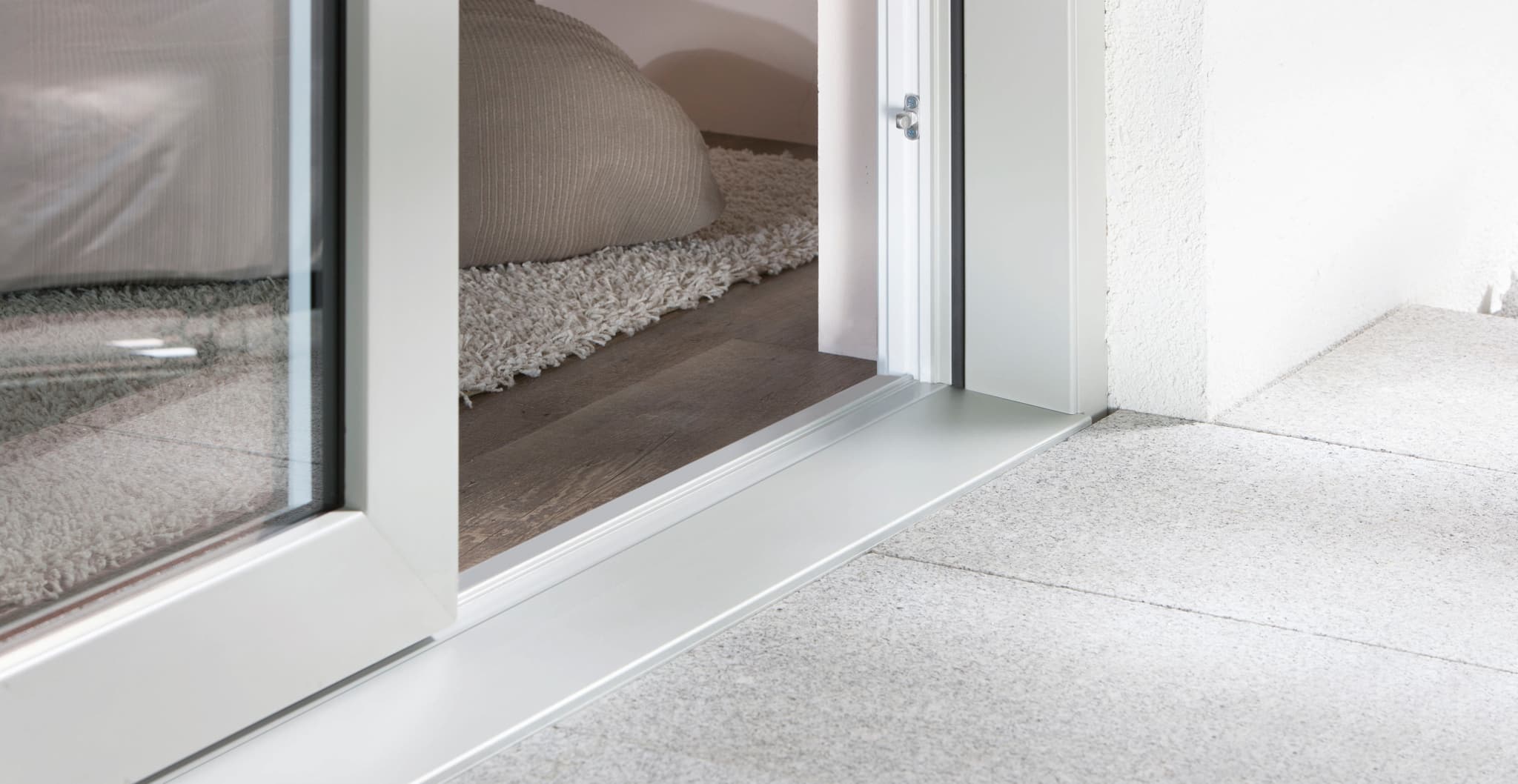 Flache Aluminium-Bodenschwelle einer geöffneten Hebeschiebetür, links Teppich im Wohnraum, rechts heller Terrassenbelag